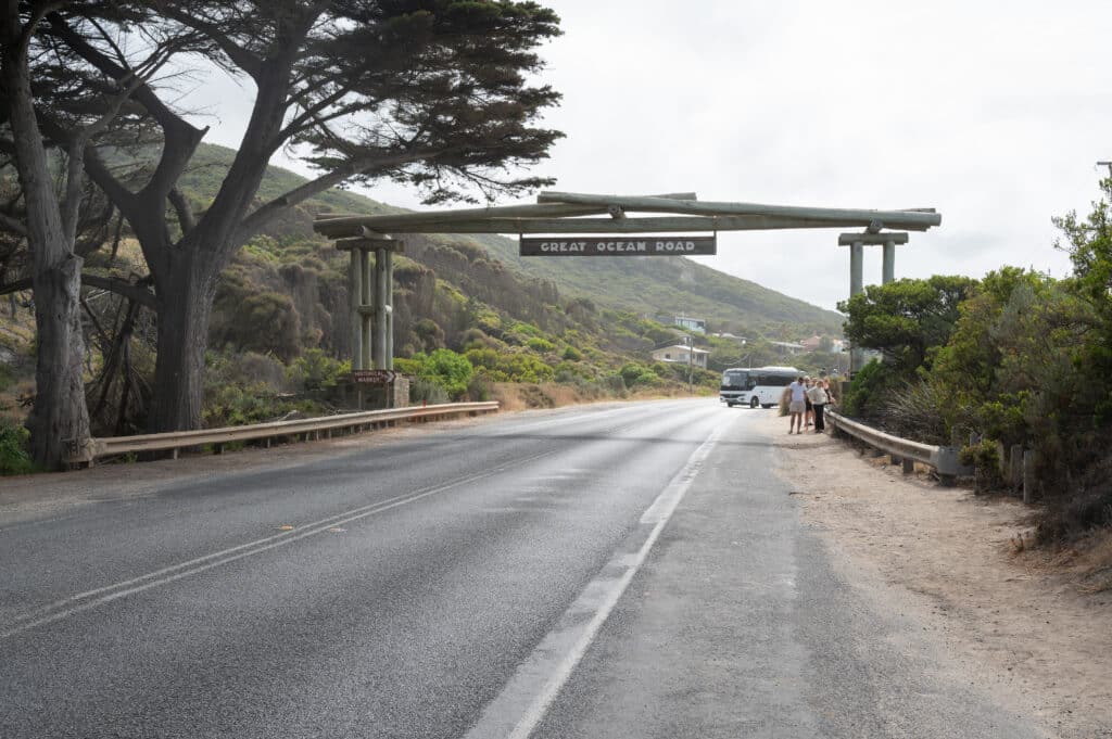 The timber Memorial Arch spans the Great Ocean Road at Eastern View, with a coach and visitors beneath its sign.