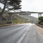 The timber Memorial Arch spans the Great Ocean Road at Eastern View, with a coach and visitors beneath its sign.