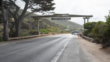 The timber Memorial Arch spans the Great Ocean Road at Eastern View, with a coach and visitors beneath its sign.