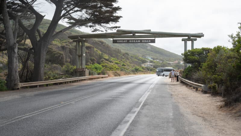 The timber Memorial Arch spans the Great Ocean Road at Eastern View, with a coach and visitors beneath its sign.