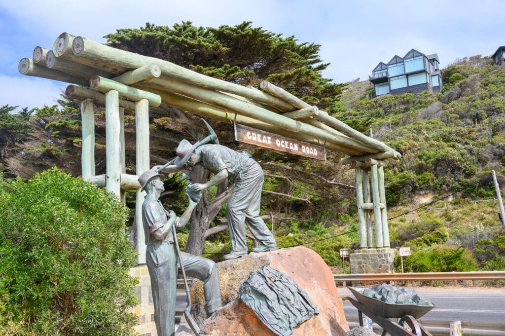 The Diggers bronze sculpture depicts two road workers beside a wheelbarrow, with the Great Ocean Road Memorial Arch behind.