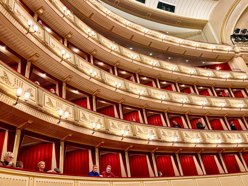 Inside a theatre with 6 tiers of curved gold balconies filled with red seat boxes