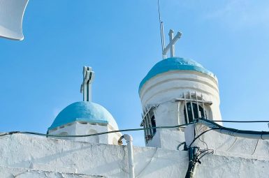 Pale blue sky. In foreground, is a white washed church with two steeples with pale blue roofs and crosses on top